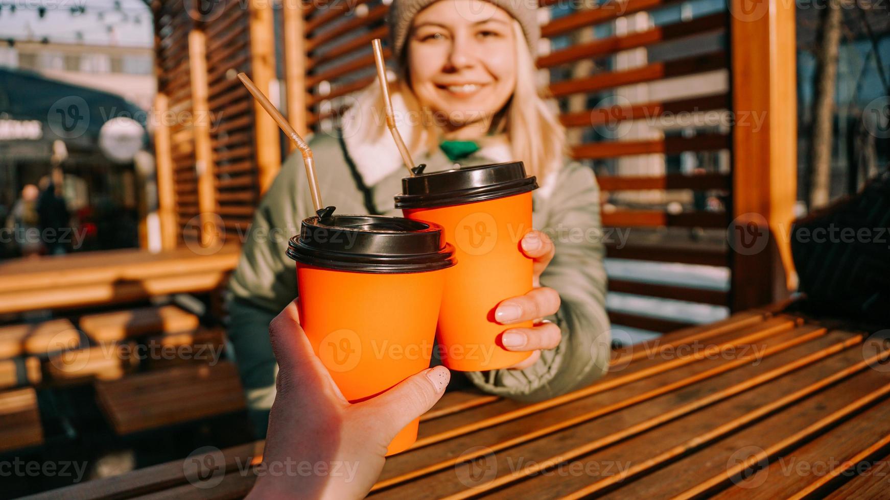 Two friends clink paper cups with mulled wine or hot tea on a sunny winter day photo
