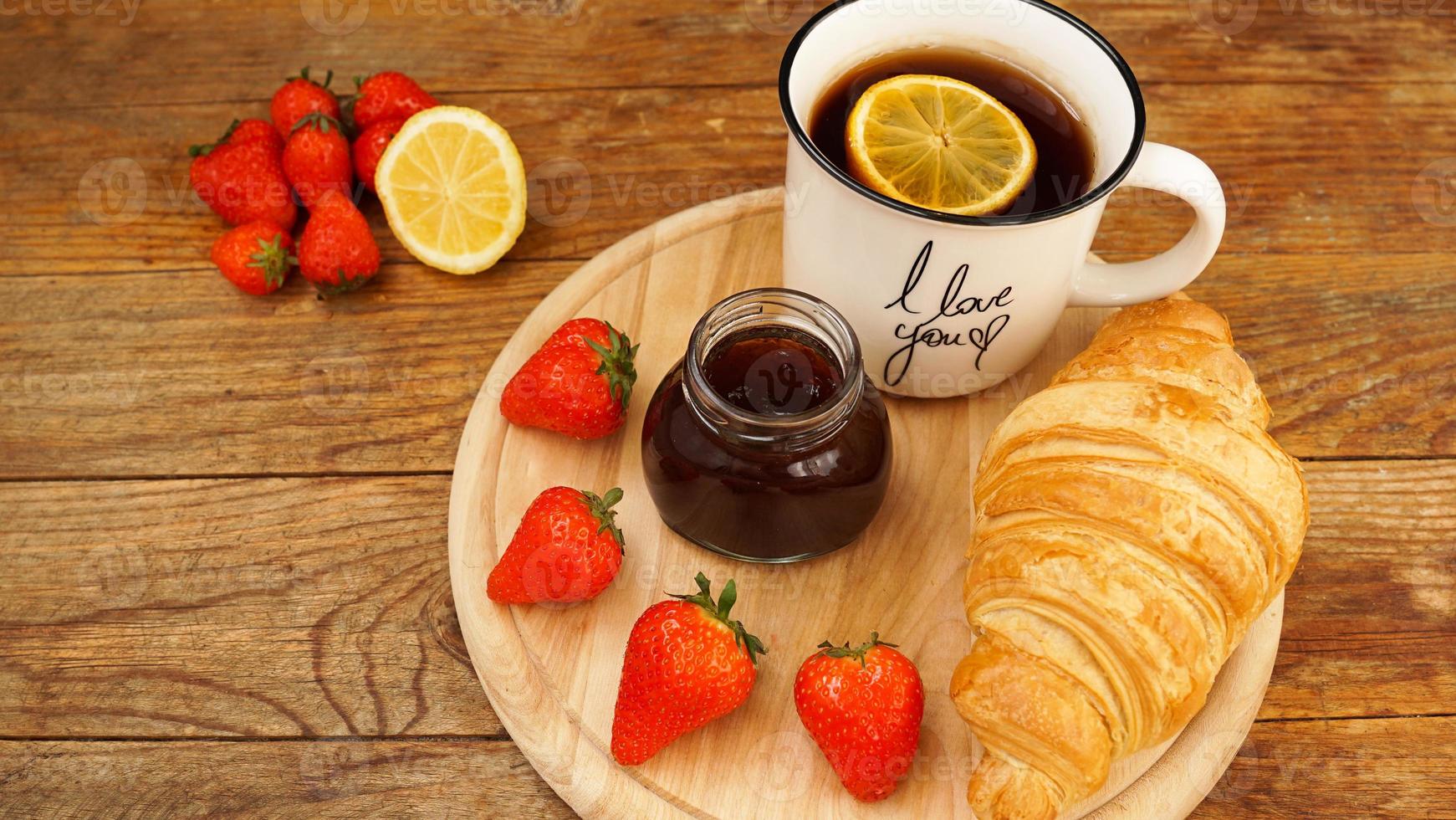 Tea break snacks. Lemon tea, croissant, jar of jam and fresh strawberries. photo