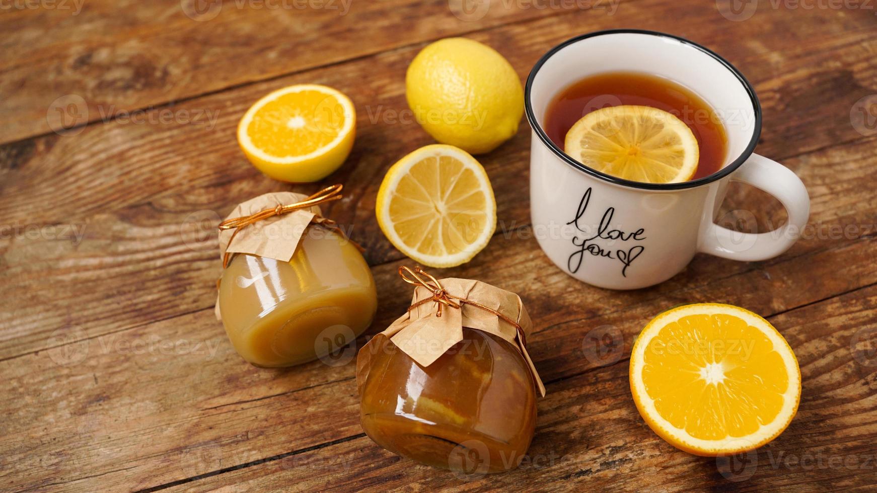 Sweet breakfast. Cup of black tea with lemon. Lemons and jars with jam photo