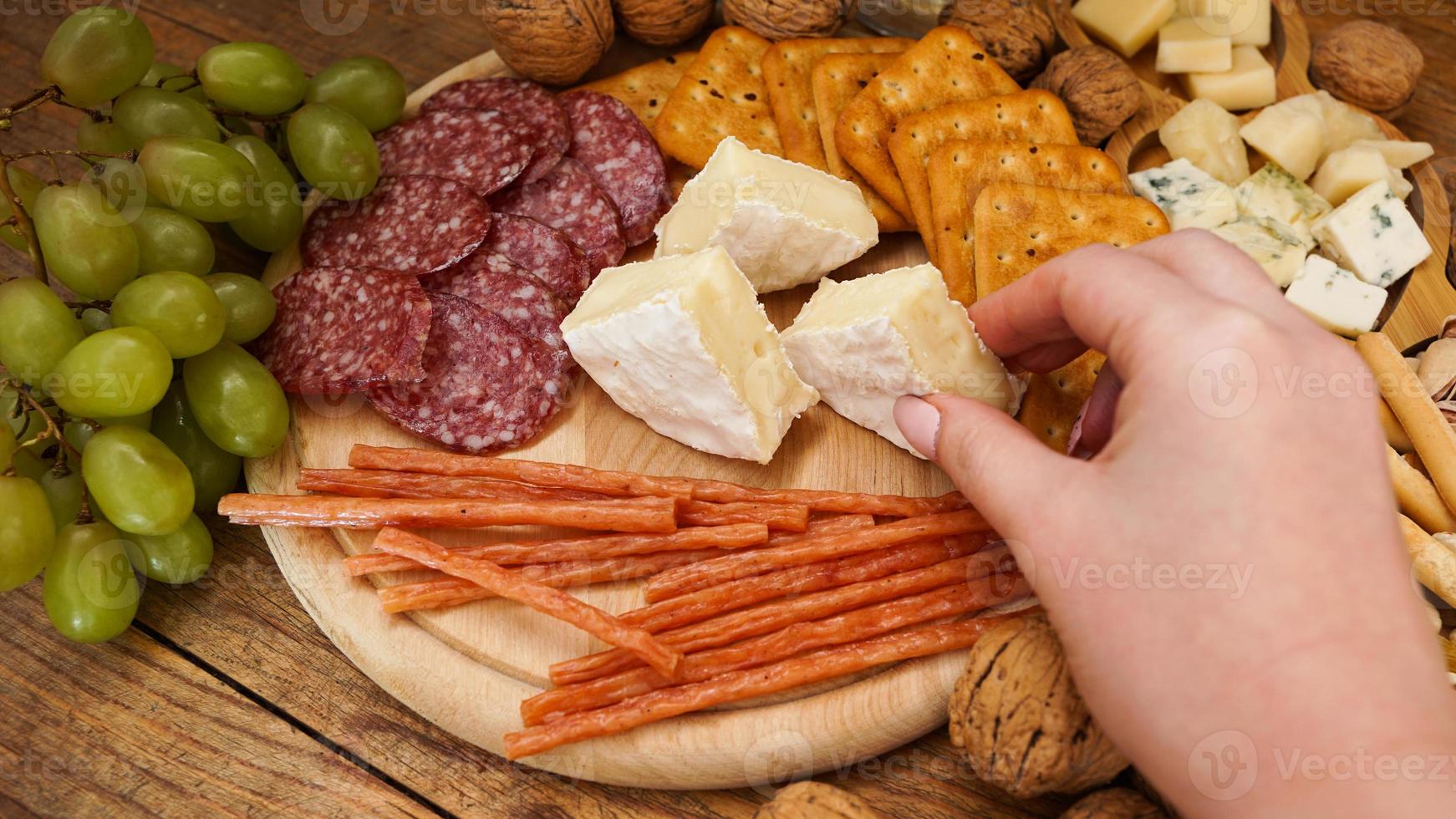 A woman hand takes a piece of Camembert cheese from a cheese plate photo