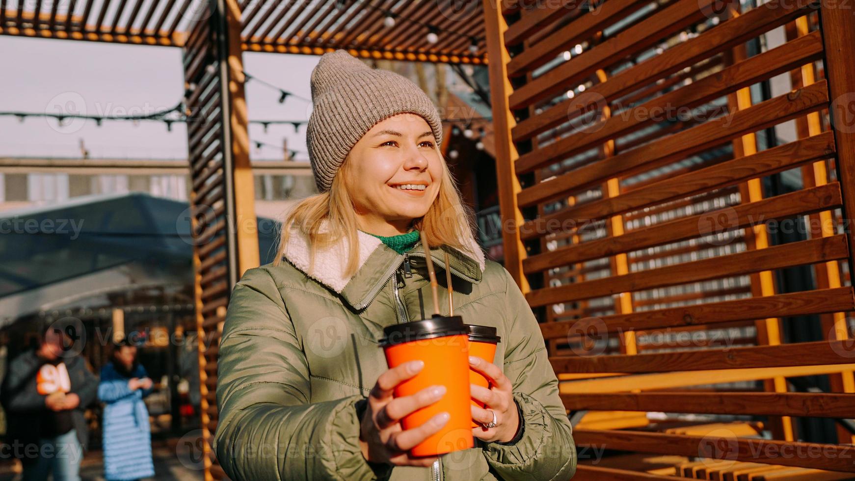 mujer lleva dos tazas de café o vino caliente en la ciudad fuera del patio de comidas foto
