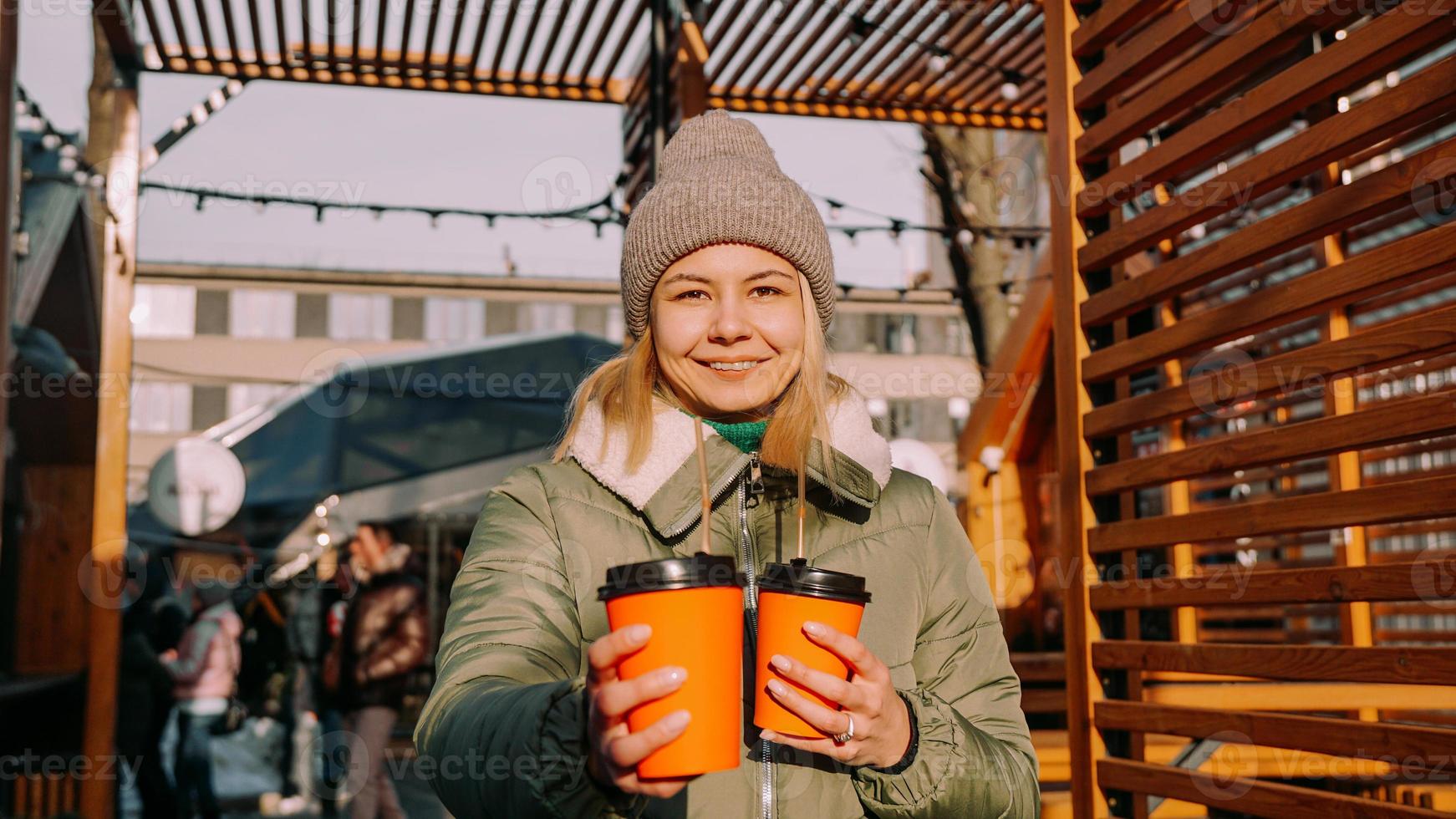 Woman carries two cups of coffee or mulled wine at the city outside food court photo