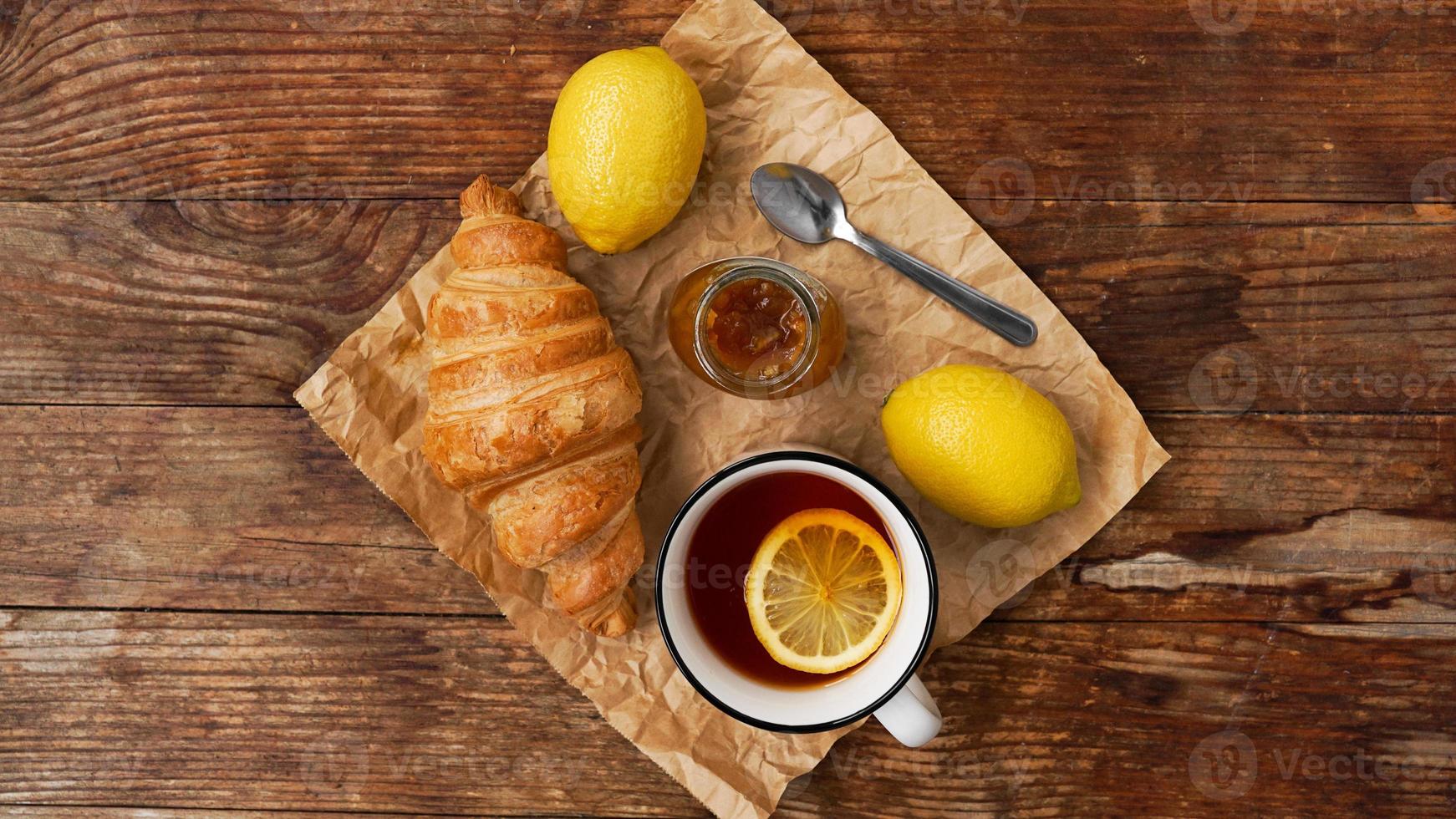 Lemon tea, home made jam, croissant on wooden table. Breakfast concept. photo