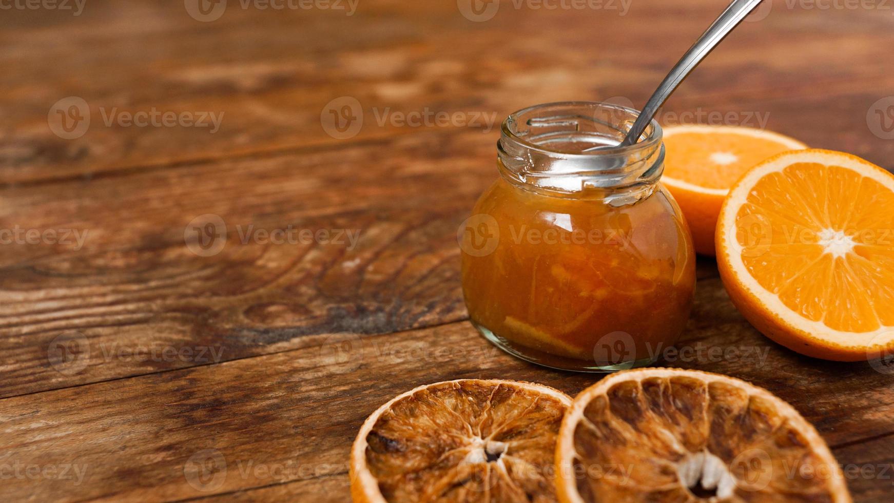 Jar of orange jam, dry oranges on wooden background from top view. photo
