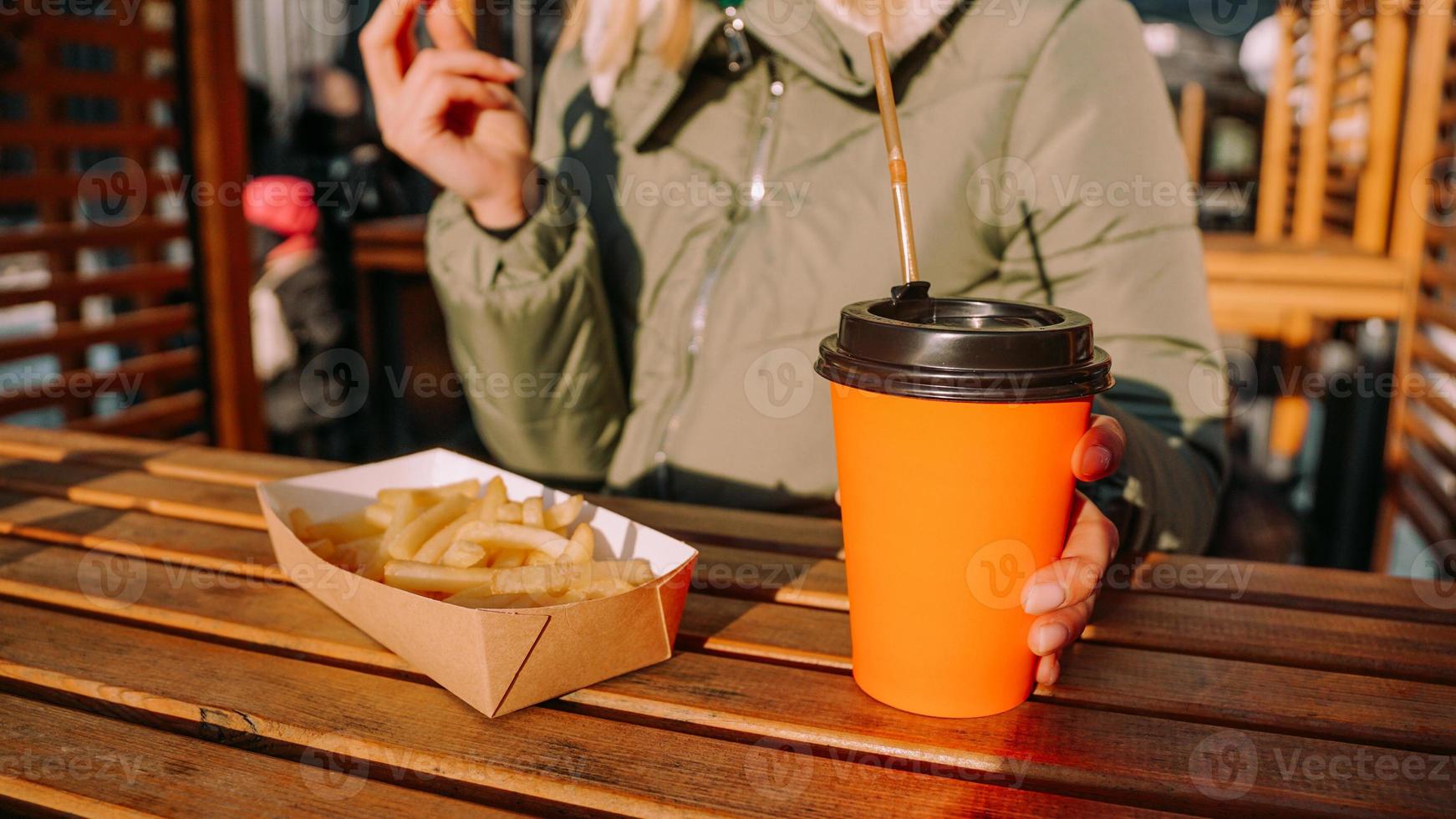 Woman eating tasty french fries and drinking tea in outdoor cafe. Close-up photo