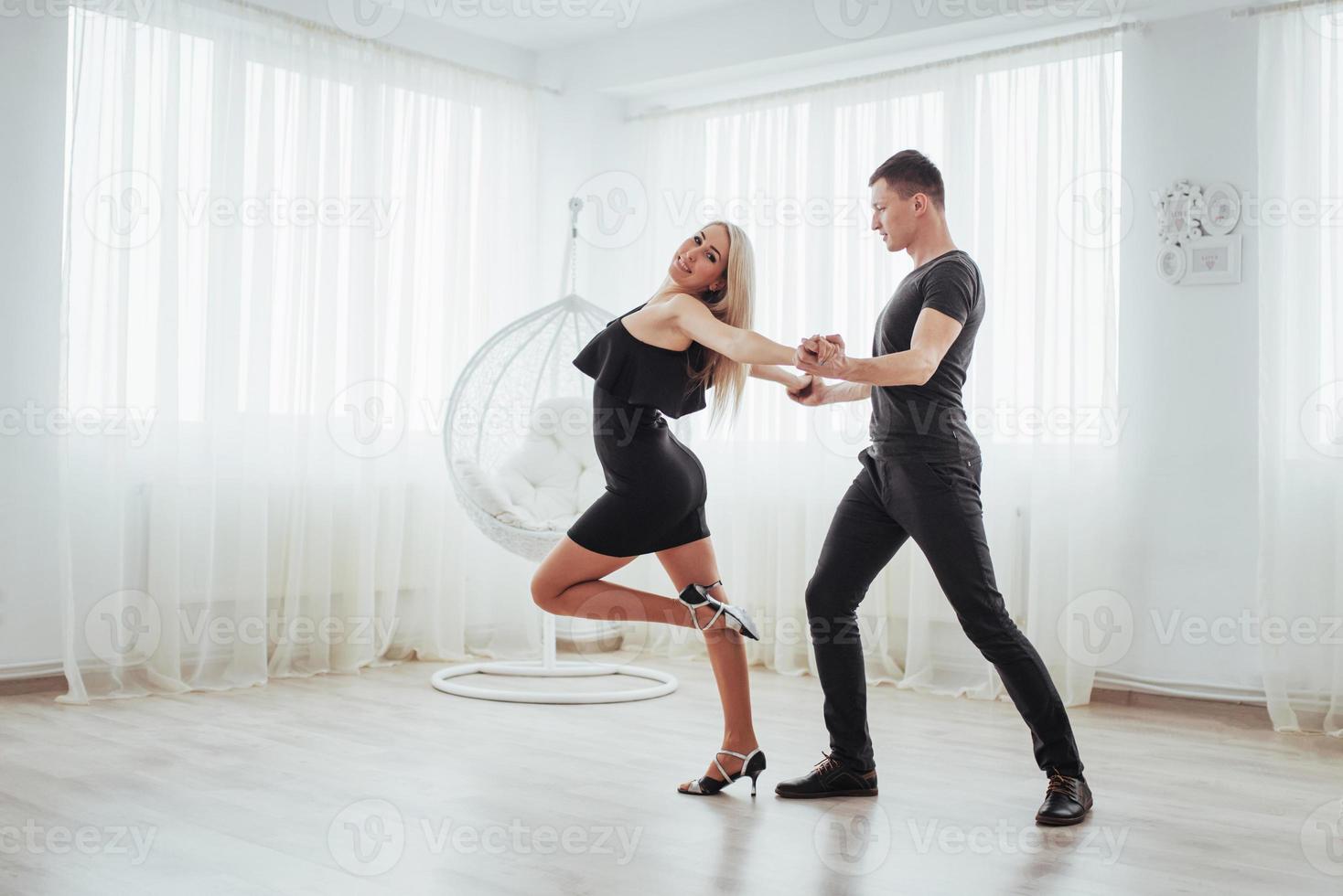 pareja joven bailando música latina. bachata, merengue, salsa. pose de dos elegancia en la habitación blanca foto