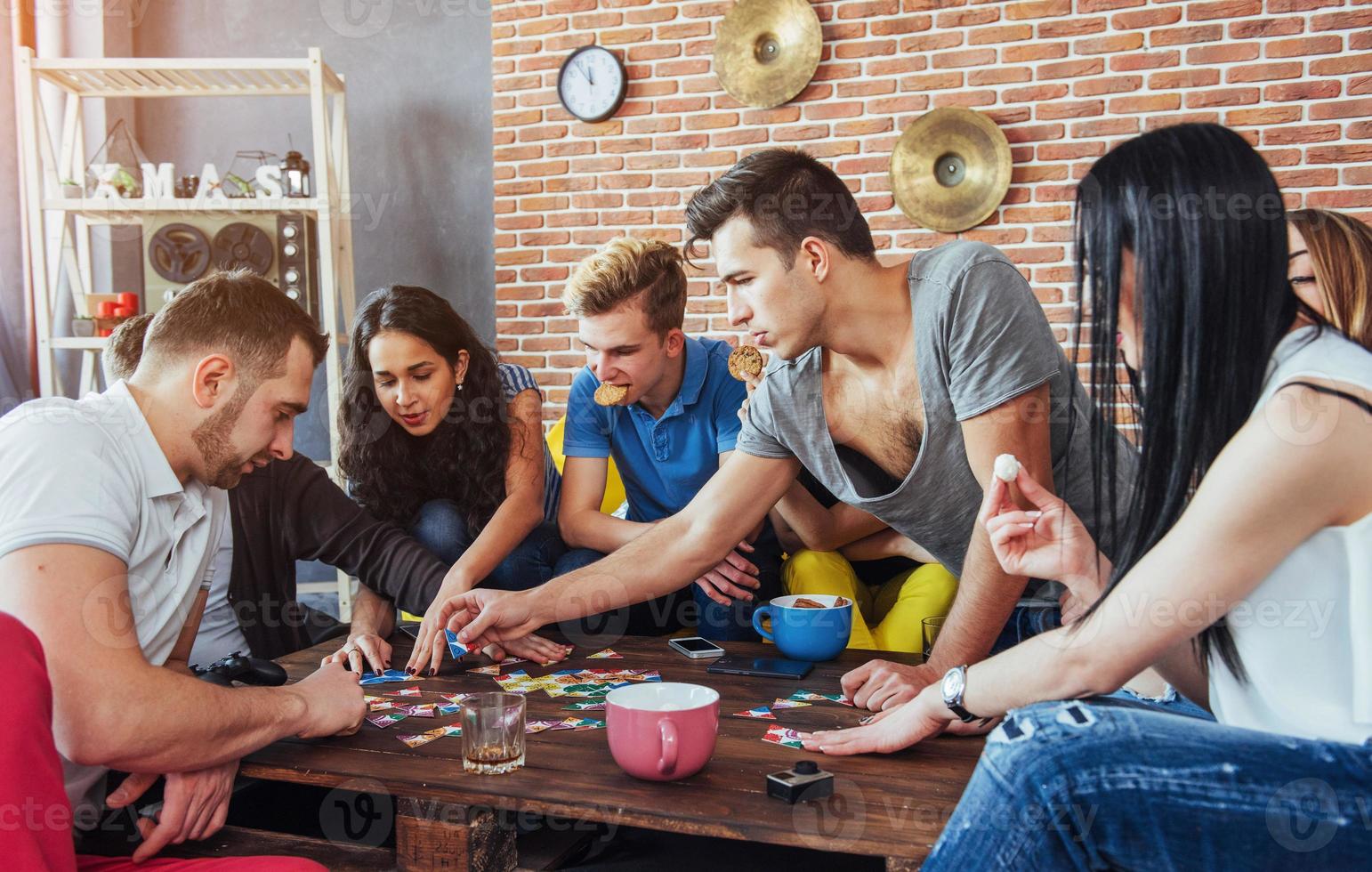 Group of creative friends sitting at wooden table. People having fun while playing board game photo