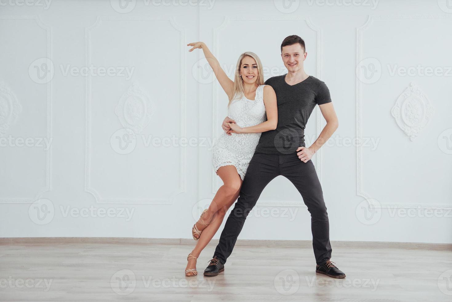 pareja joven bailando música latina. bachata, merengue, salsa. pose de dos elegancia en la habitación blanca foto