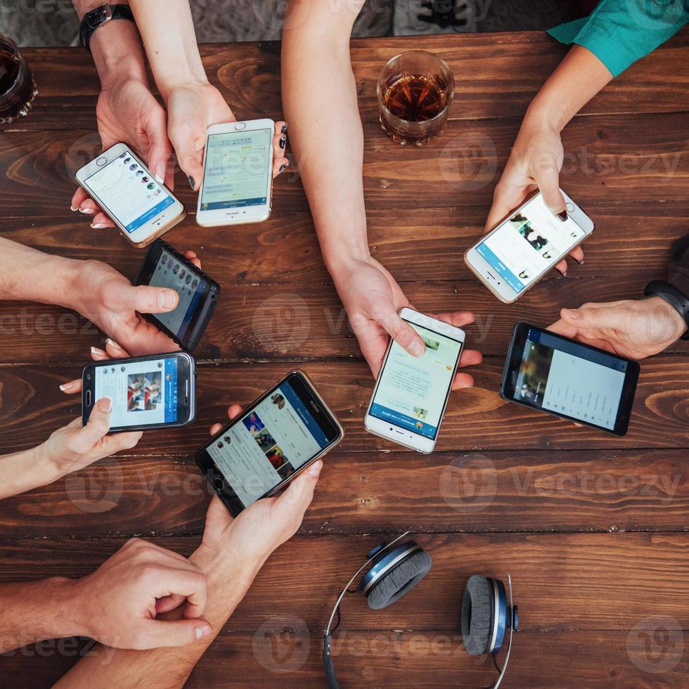 Top view hands circle using phone in cafe - Multiracial friends mobile addicted interior scene from above - Wifi connected people in bar table meeting - Concept of teamwork photo