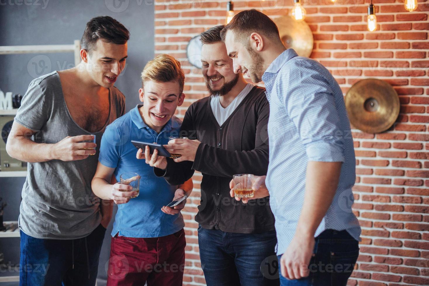 Cheerful old friends communicate with each other and phone watch,  glasses of whiskey in pub. Concept  entertainment  lifestyle. Wifi connected people in bar table meeting photo