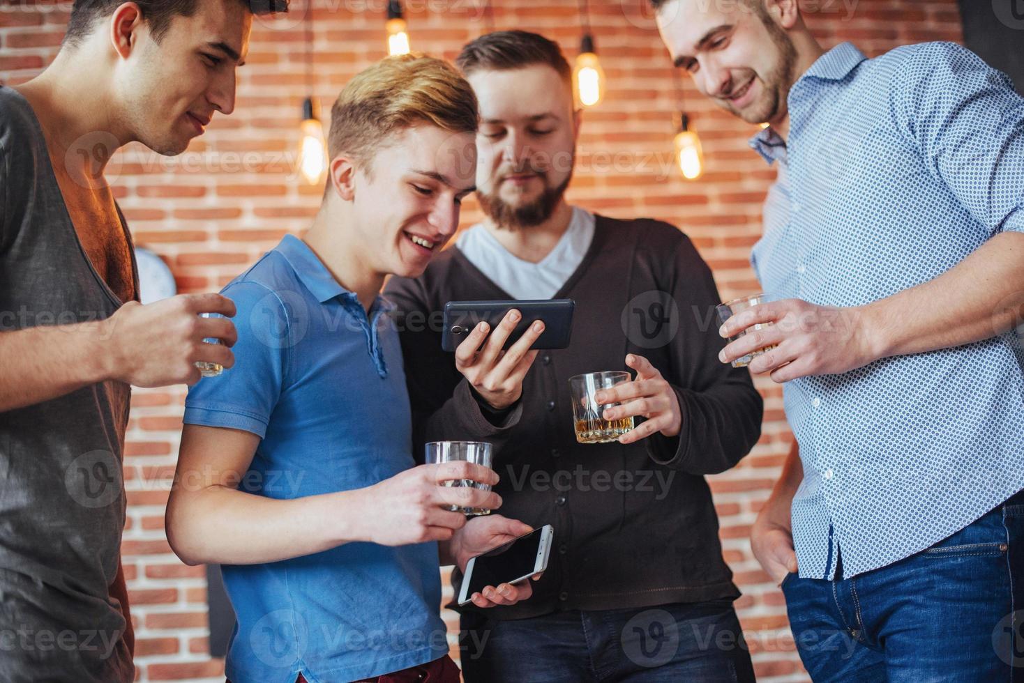 Cheerful old friends communicate with each other and phone watch,  glasses of whiskey in pub. Concept  entertainment  lifestyle. Wifi connected people in bar table meeting photo