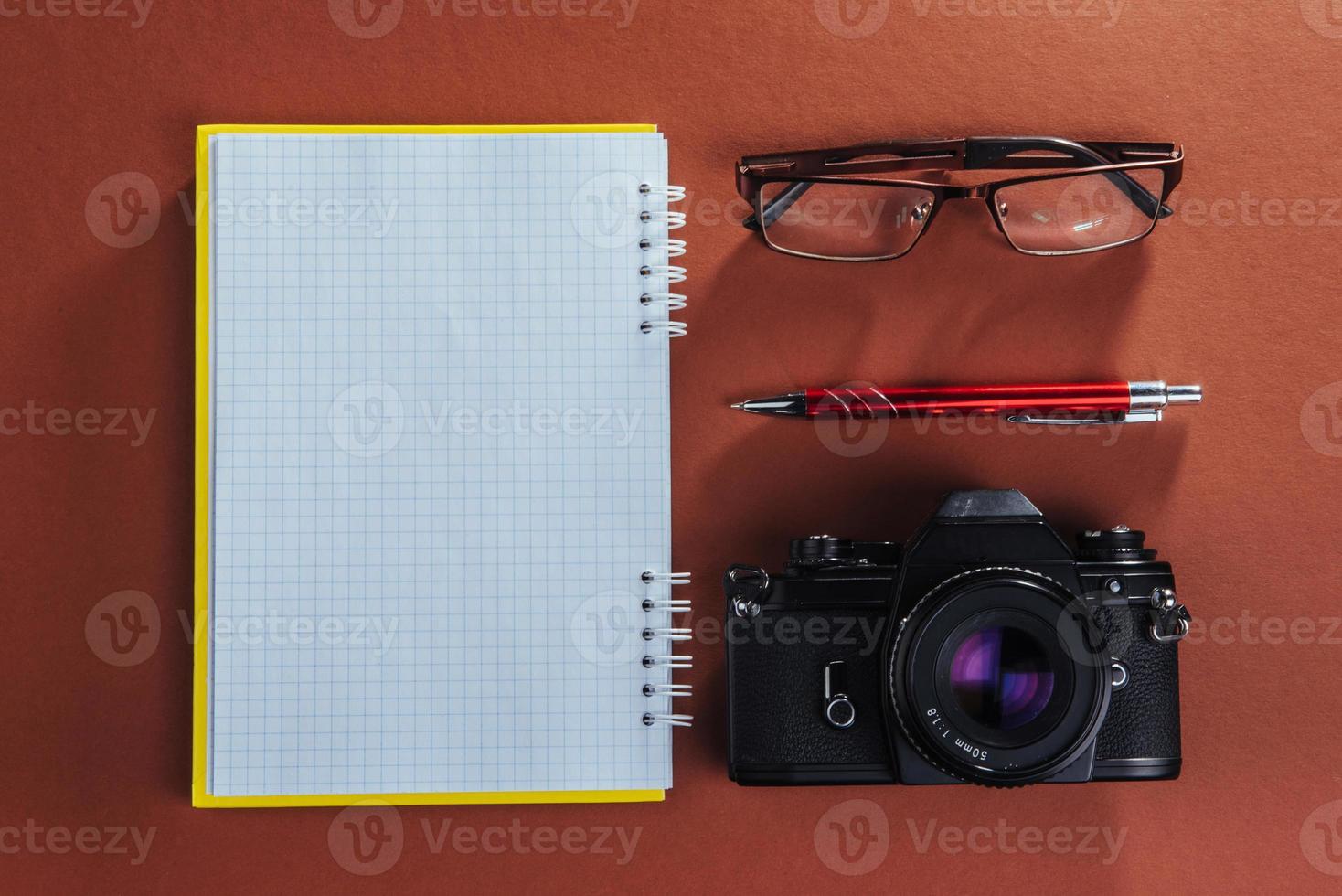 camera, glasses and notepad and pencil on a brown wooden background photo