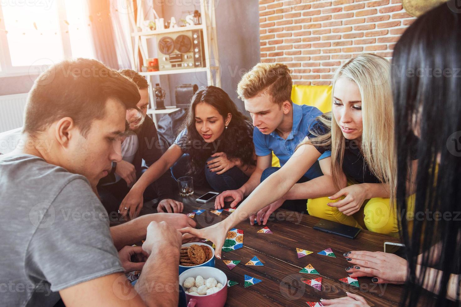 Group of creative friends sitting at wooden table. People having fun while playing board game photo