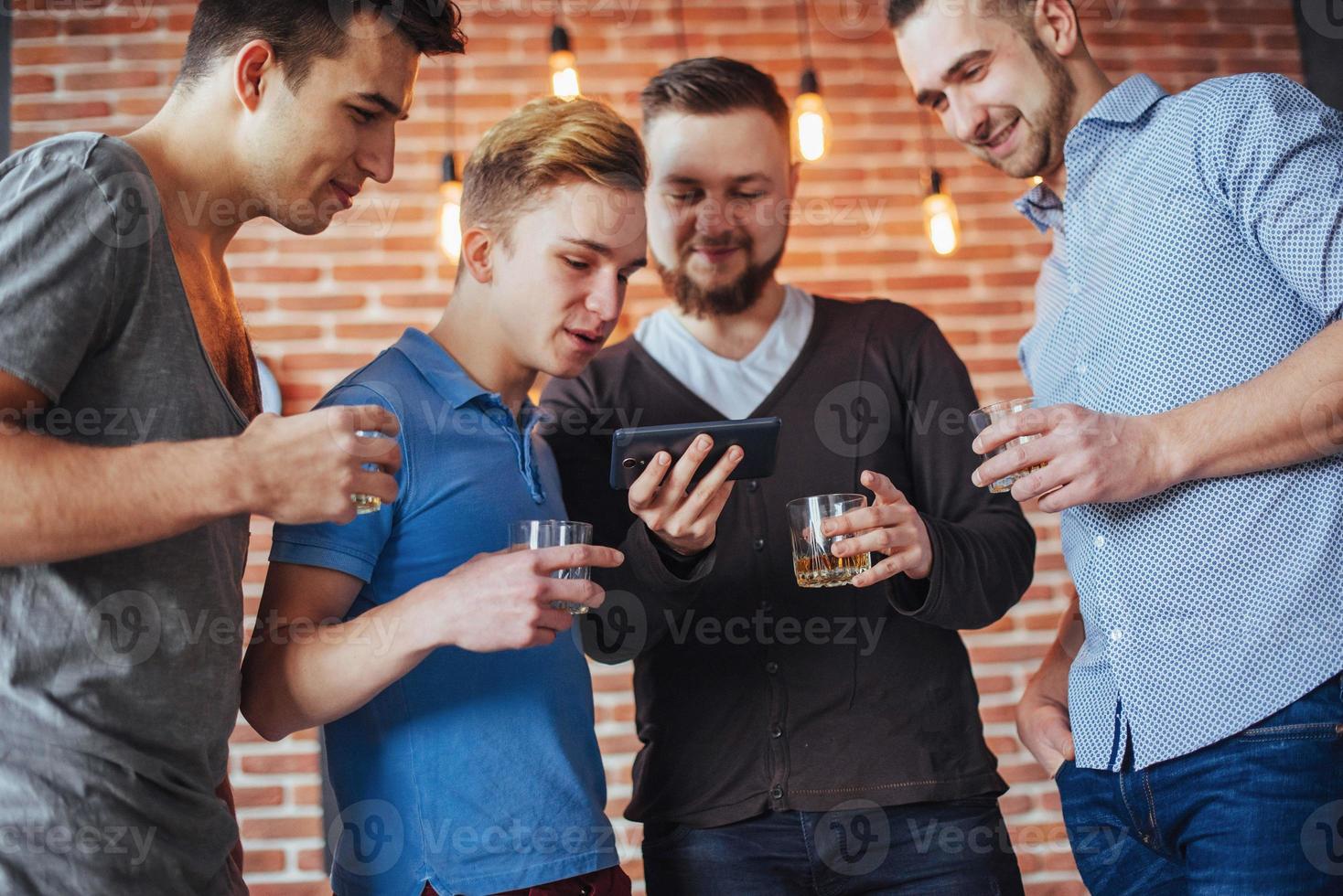 Cheerful old friends communicate with each other and phone watch,  glasses of whiskey in pub. Concept  entertainment  lifestyle. Wifi connected people in bar table meeting photo