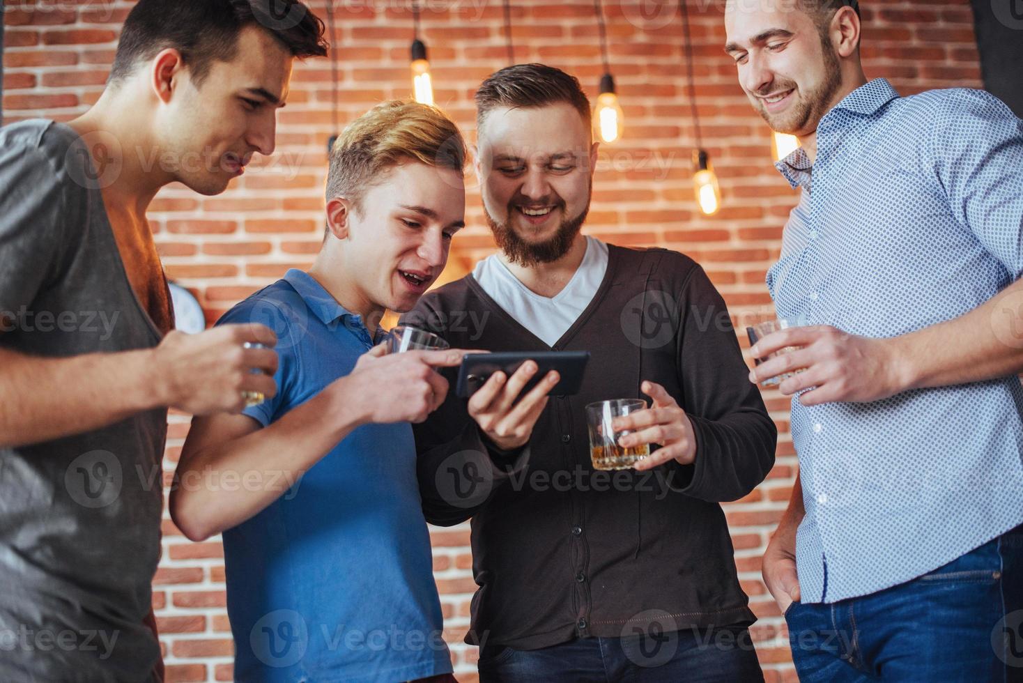 Cheerful old friends communicate with each other and phone watch,  glasses of whiskey in pub. Concept  entertainment  lifestyle. Wifi connected people in bar table meeting photo