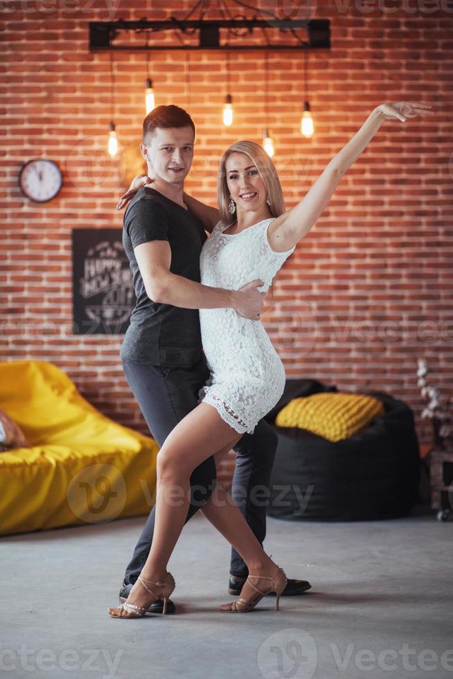 Young couple dancing latin music. Bachata, merengue, salsa. Two elegance pose on cafe with brick walls photo