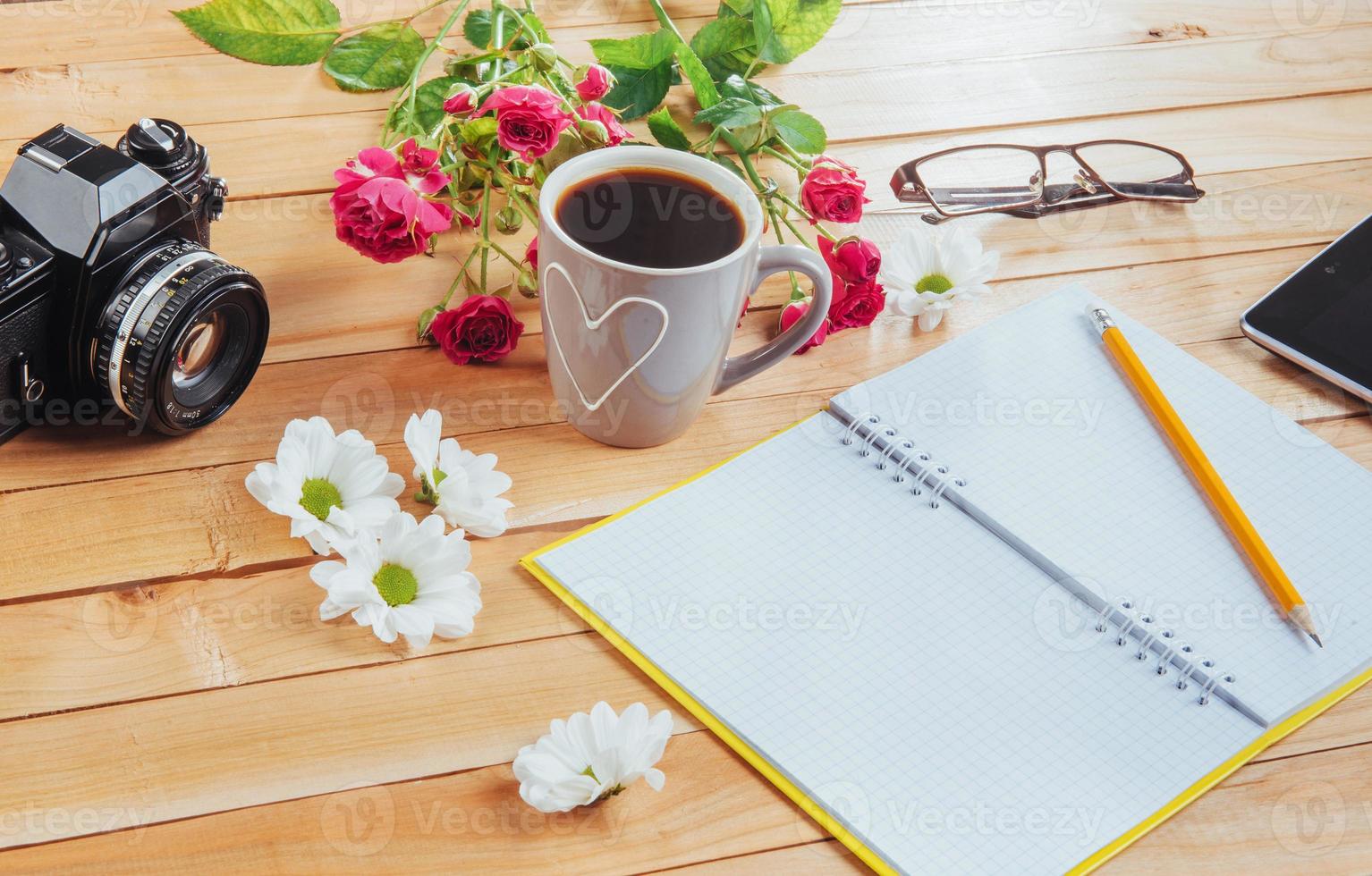 On wooden background notebook pencil, coffee and flowers. photo