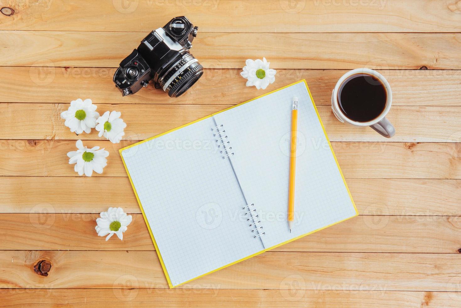 On wooden background notebook pencil, coffee and flowers. photo