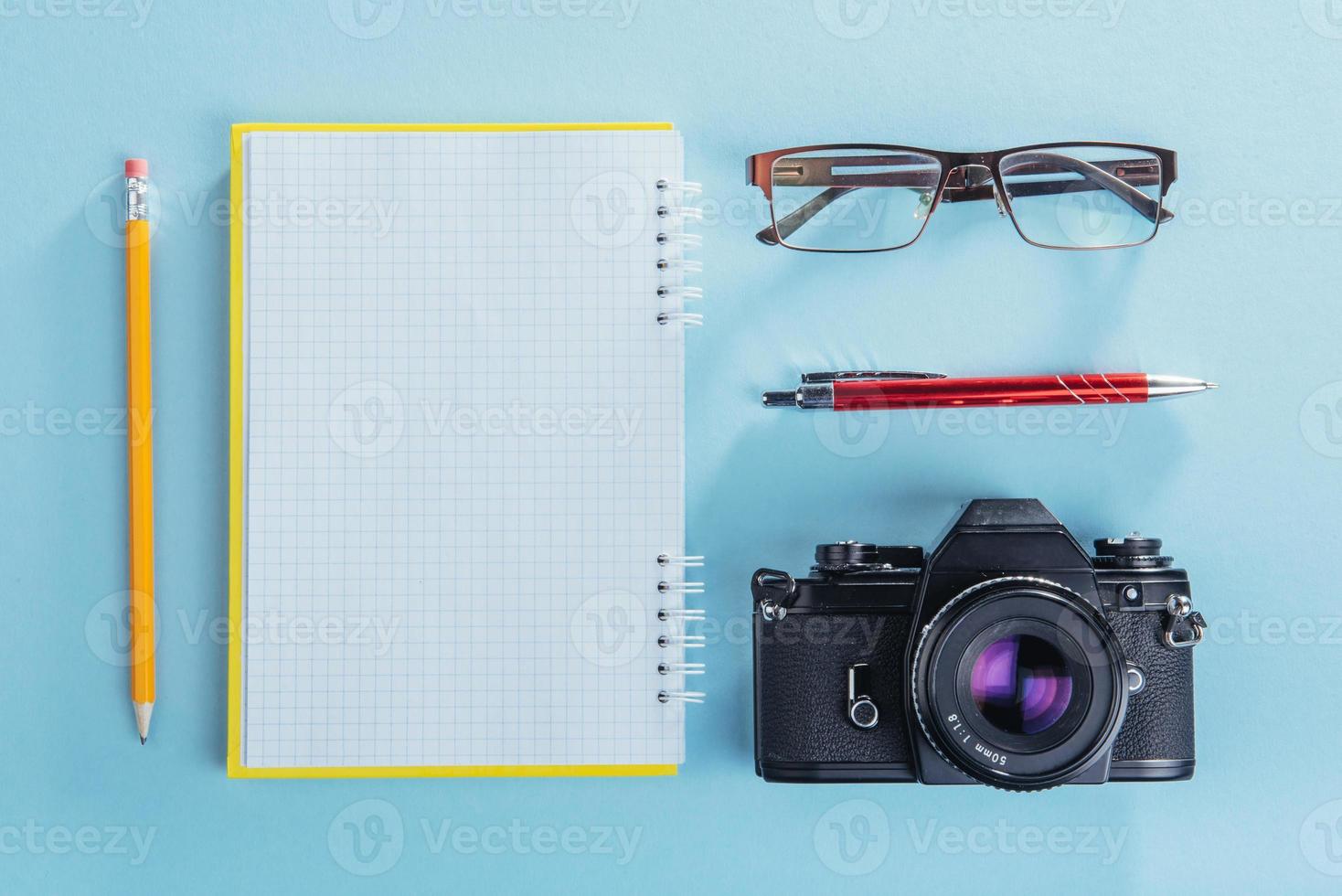 cámara, anteojos y bloc de notas y lápiz sobre un fondo de madera marrón foto