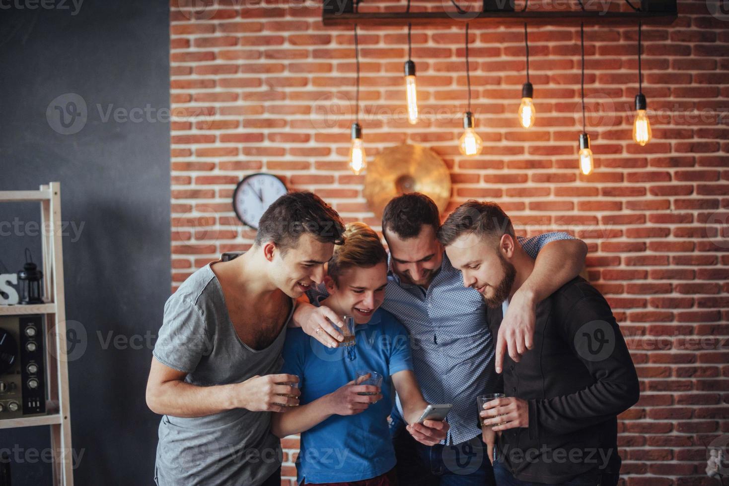 Cheerful old friends communicate with each other and phone watch,  glasses of whiskey in pub. Concept  entertainment  lifestyle. Wifi connected people in bar table meeting photo