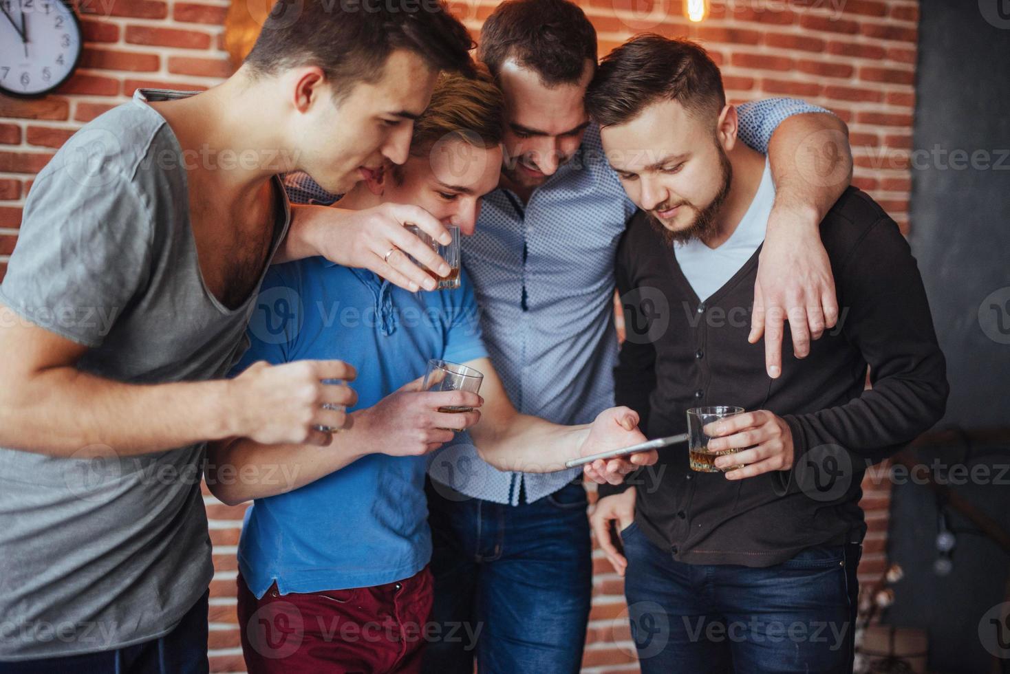 Cheerful old friends communicate with each other and phone watch,  glasses of whiskey in pub. Concept  entertainment  lifestyle. Wifi connected people in bar table meeting photo