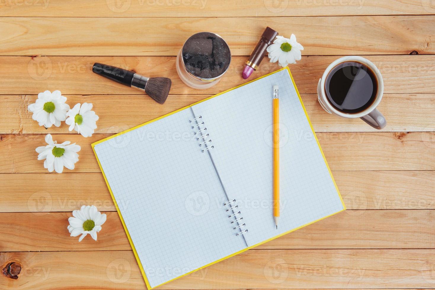 On wooden background notebook pencil, coffee and flowers. photo