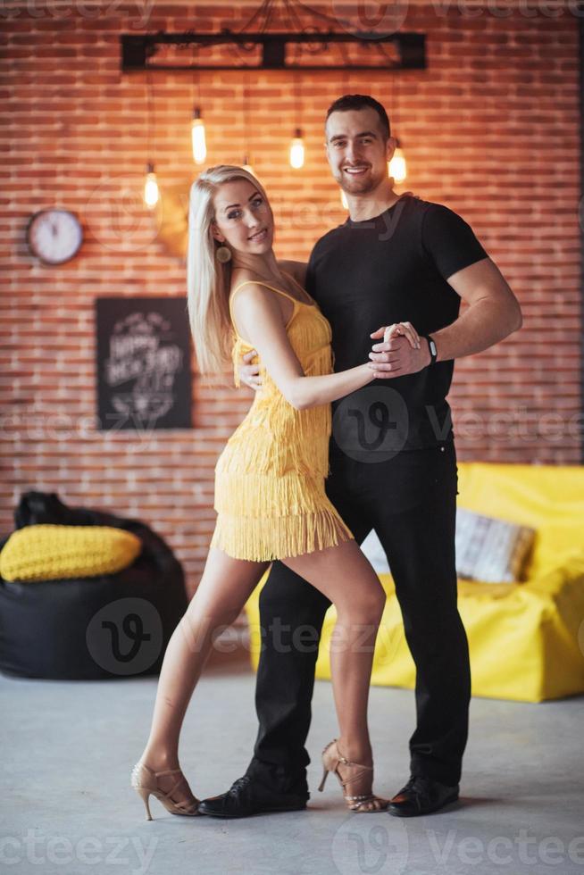 pareja joven bailando música latina bachata, merengue, salsa. pose de dos elegancia en el café con paredes de ladrillo foto