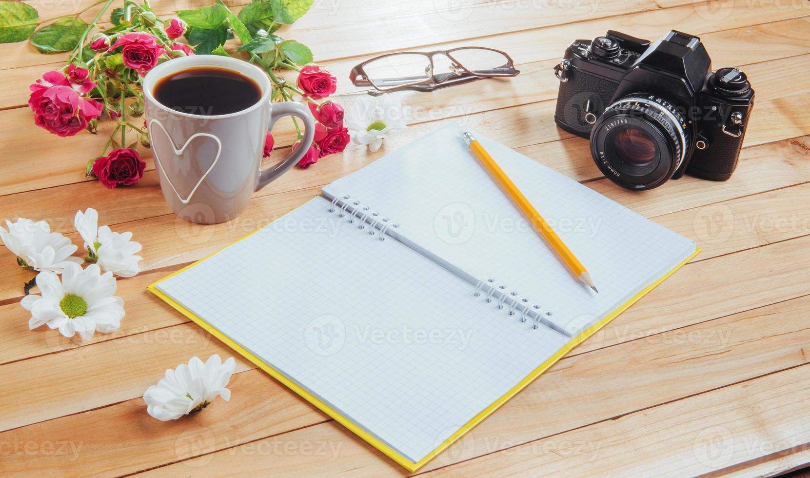 camera, glasses and notepad and pencil on a brown wooden background photo