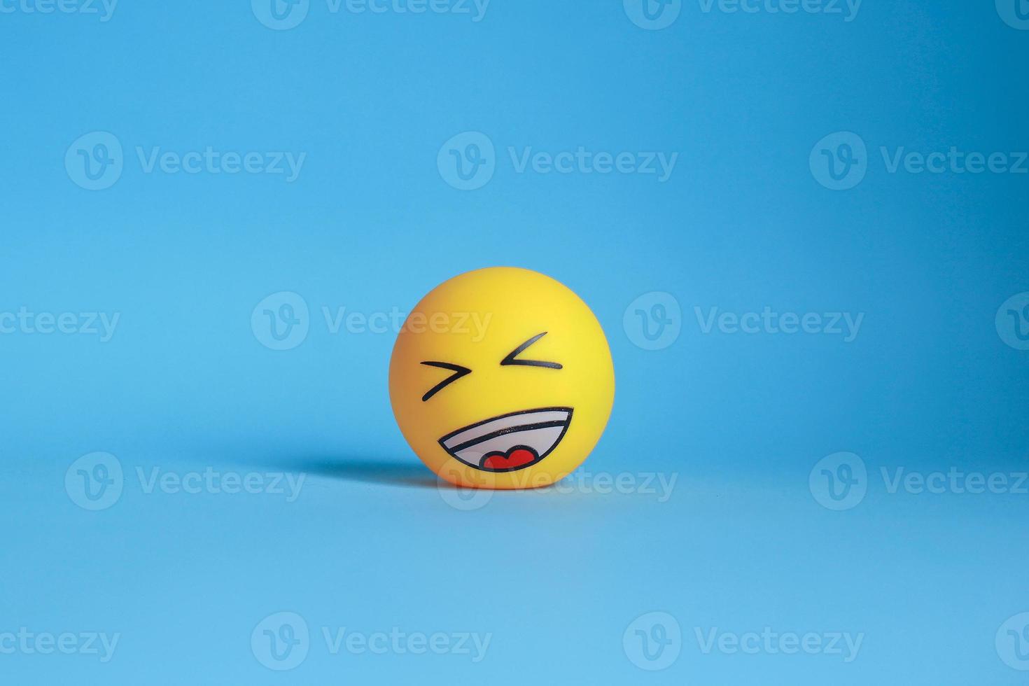 Round yellow face with expression laughing out loud while closing eyes isolated on blue background. laughing emoji photo