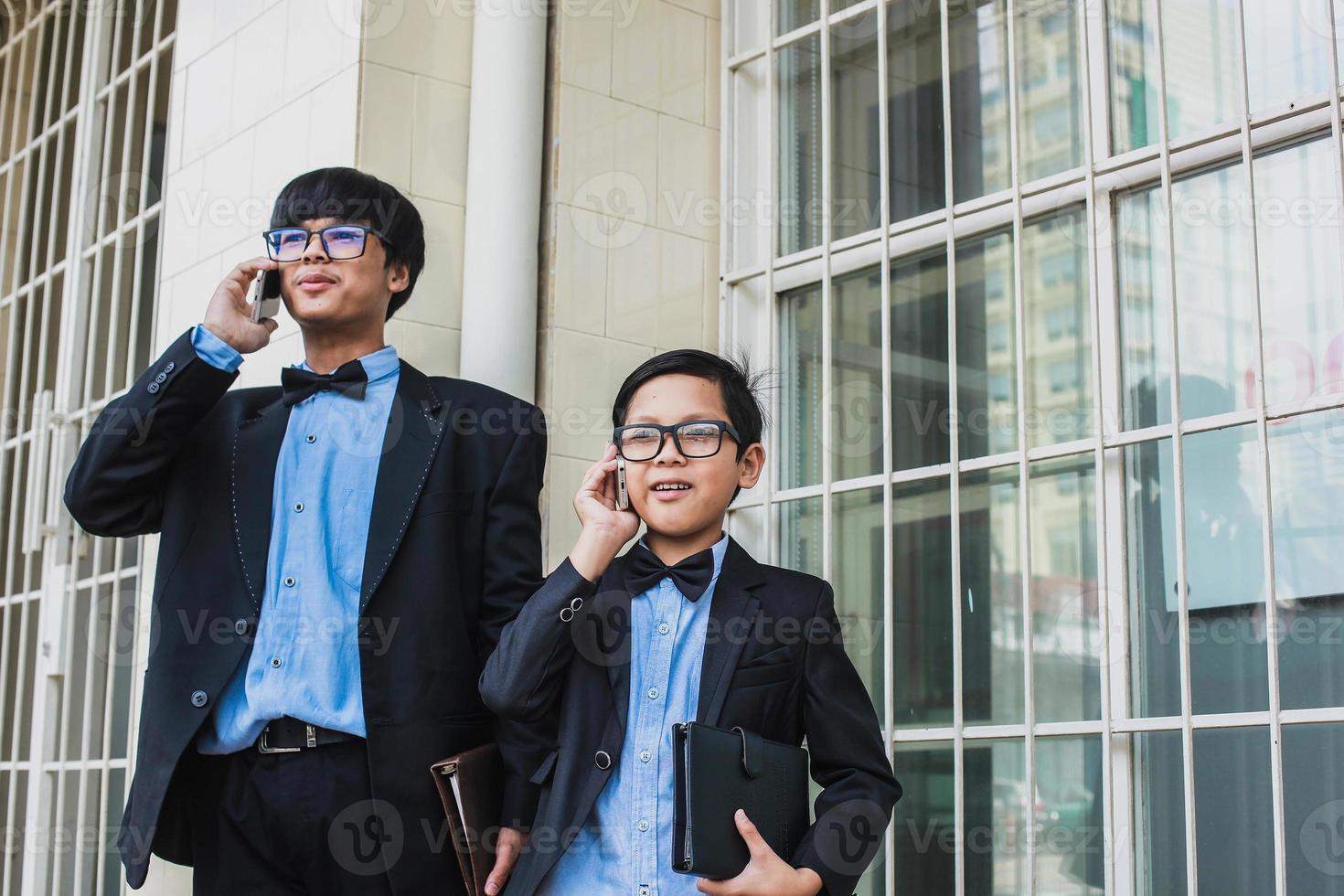 Two teenager with vintage black suit  are talking on the phone while smiling and holding notebook photo