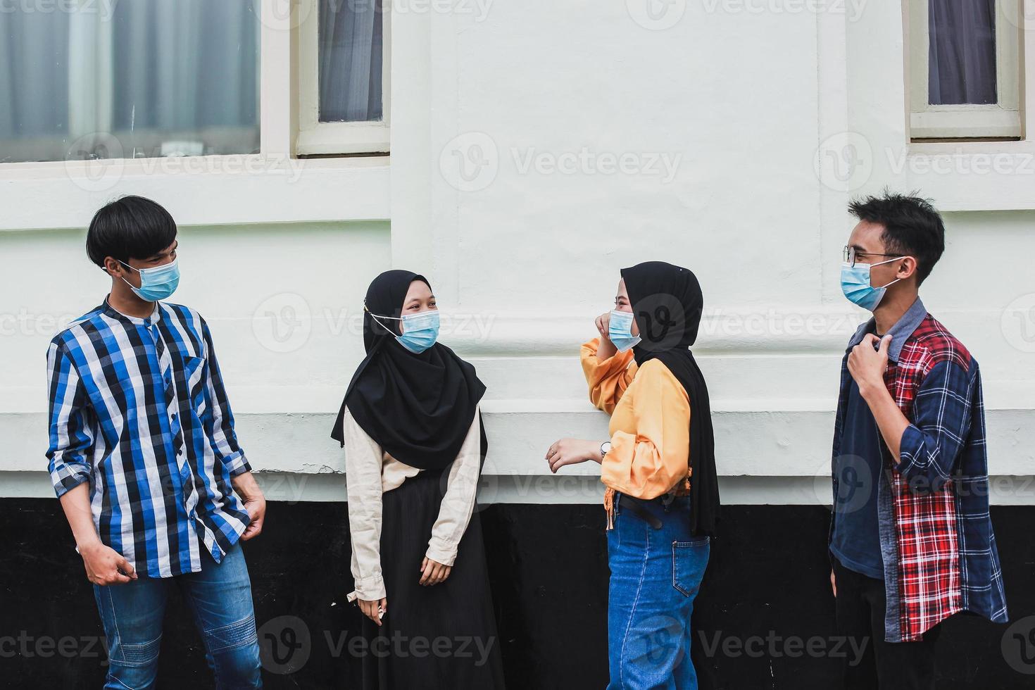 Group of young people wearing protective masks to protect themselves from the coronavirus smiling and talking together with distance photo