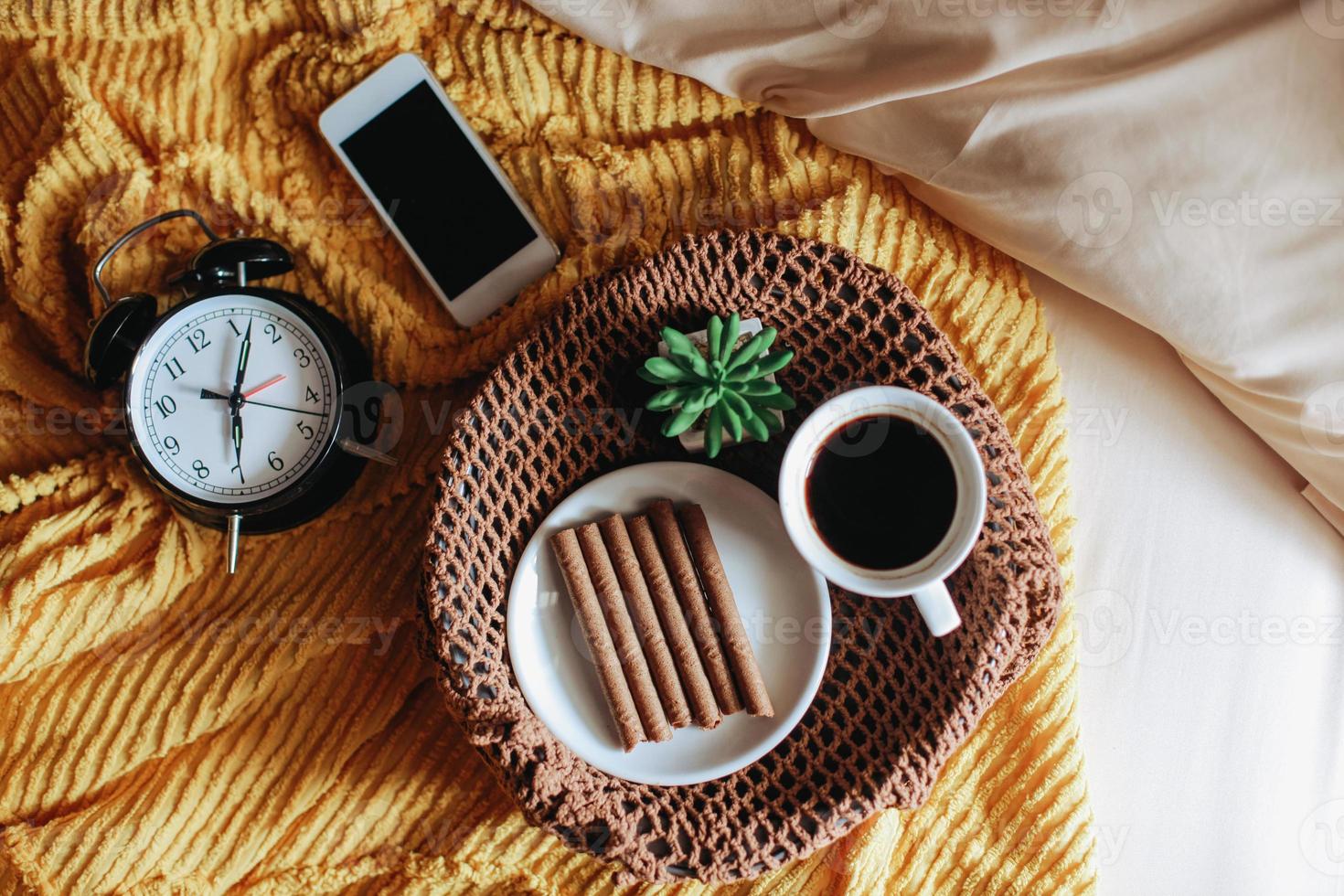 sabroso refrigerio y una taza de café para el desayuno con un reloj que muestra las 7 en punto en la cama foto