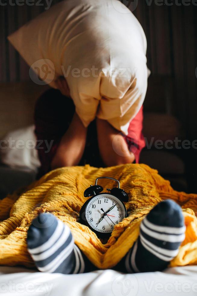 People are awakened from sleep by the alarm clock showing 7 o'clock and cover their ears with pillows photo