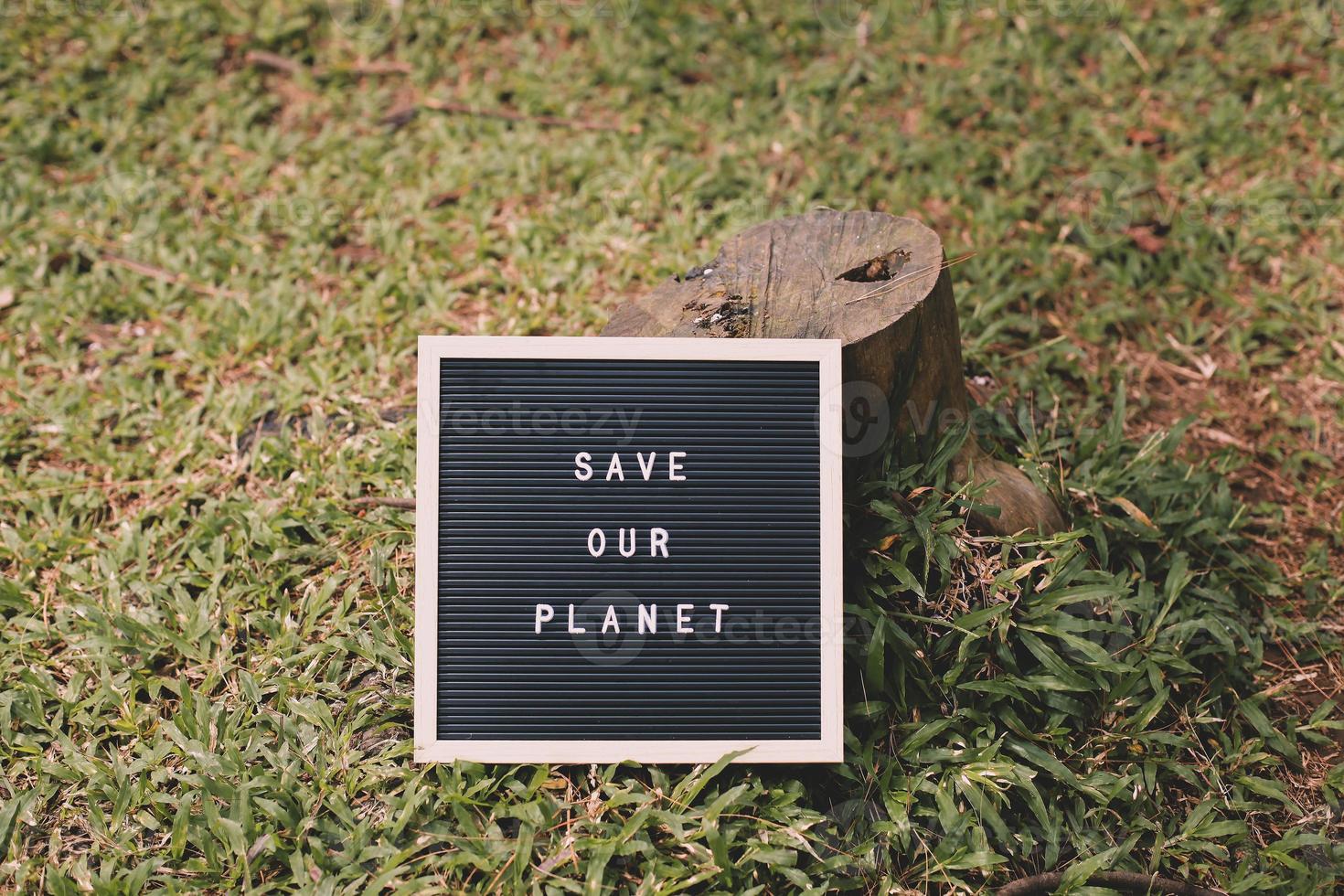 árbol talado y cita en el tablero de cartas dice salvar nuestro planeta sobre fondo de hierba verde foto