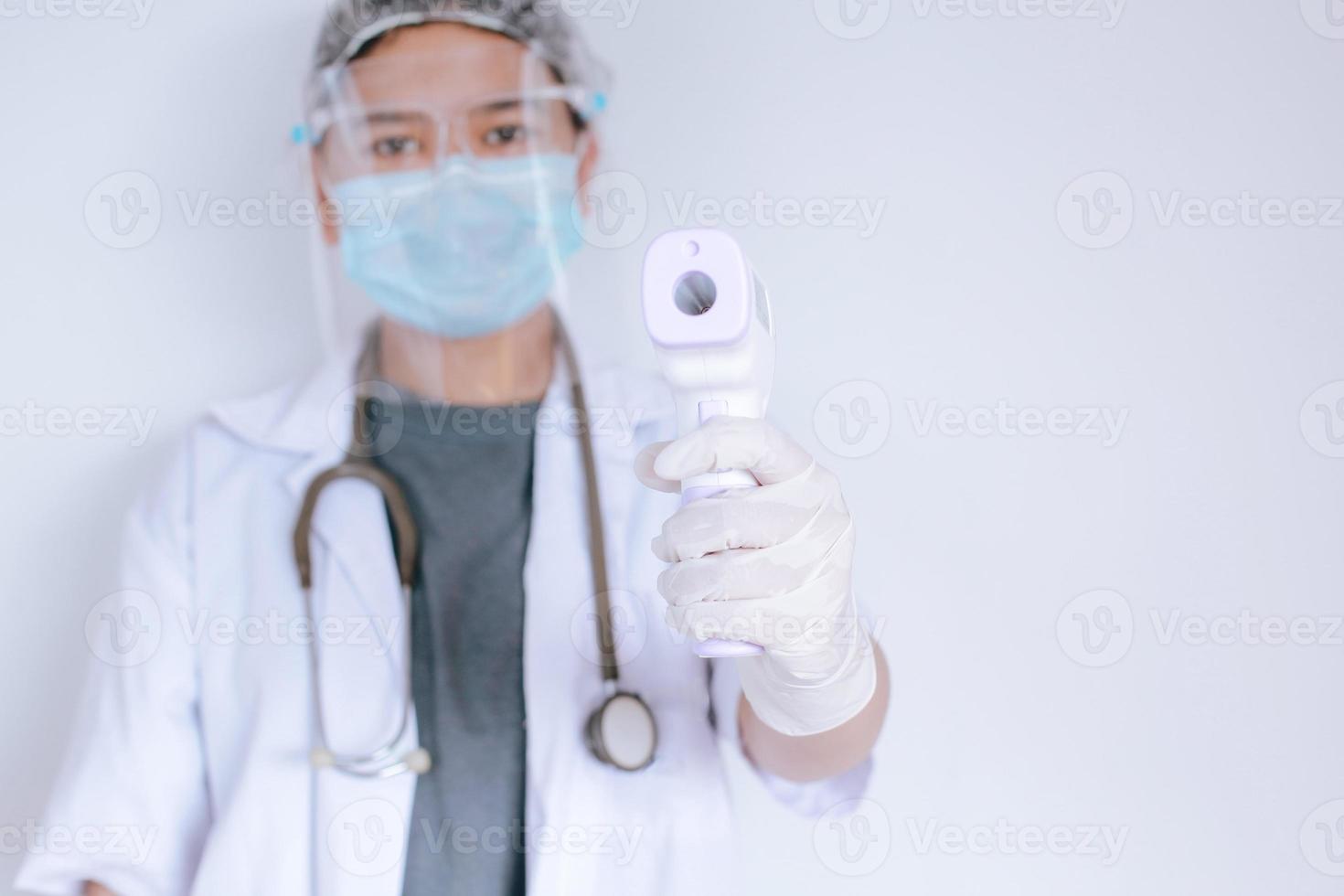 toma de primer plano de un médico que usa una máscara protectora lista para usar un termómetro de frente infrarrojo o una pistola de termómetro para verificar la temperatura corporal en busca de síntomas de virus y brotes de virus epidémicos foto