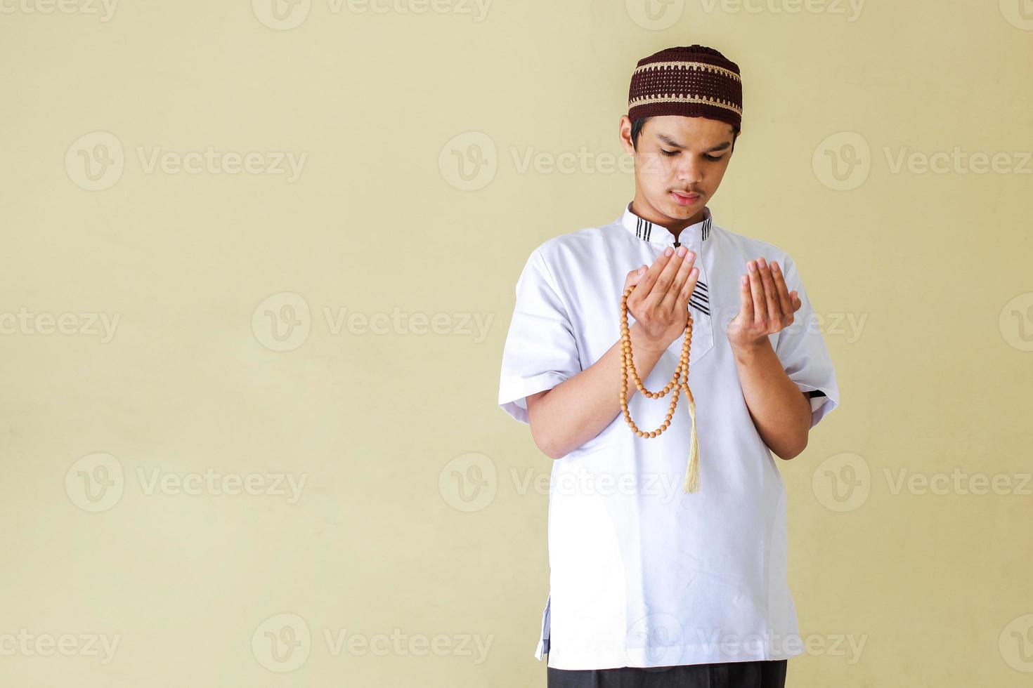 Young asian muslim man praying while holding rosary beads with copy space photo