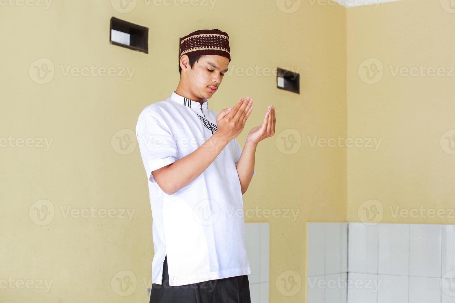 Portrait of young asian muslim man praying by raising his hands photo