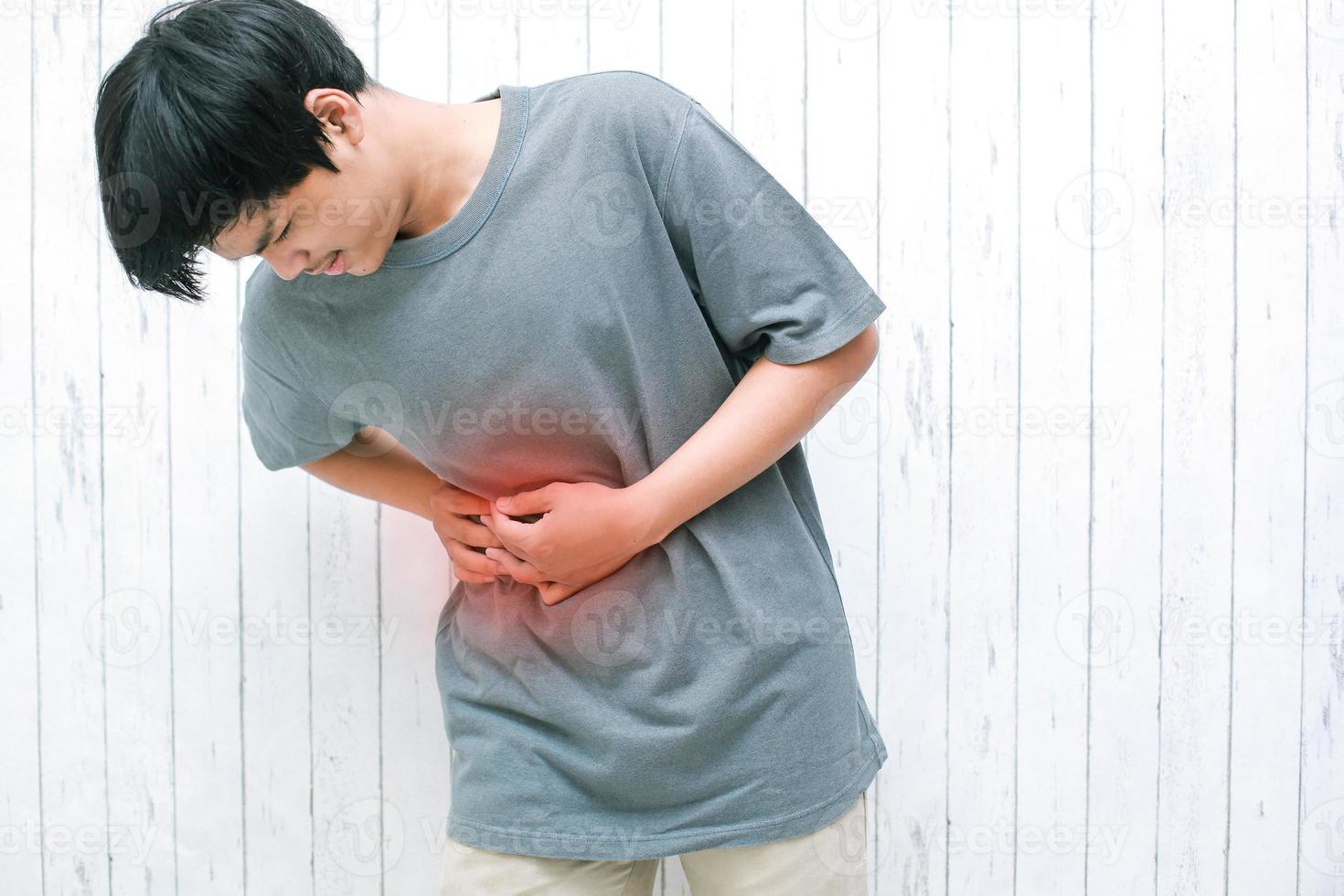 joven asiático tocando el estómago doloroso que sufre de dolor de estómago causas de úlcera gástrica, apendicitis o enfermedad del sistema gastrointestinal. foto