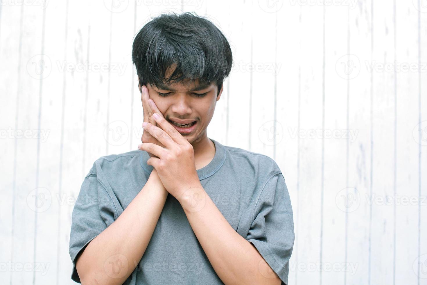 Tooth pain. Young man suffering from terrible strong teeth pain, touching cheek with hand. Male feeling painful toothache. photo