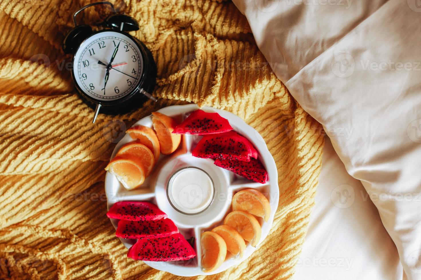 Various fruit for breakfast with clock showing 7 o'clock on the bed photo