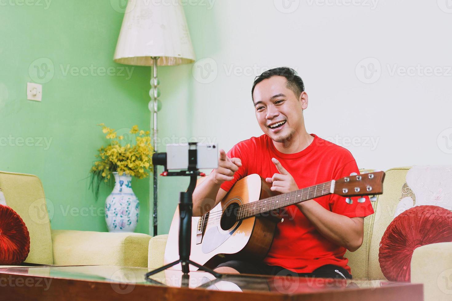 Asian man youtuber making content with a guitar while pointing his finger to the audience on smart phone photo