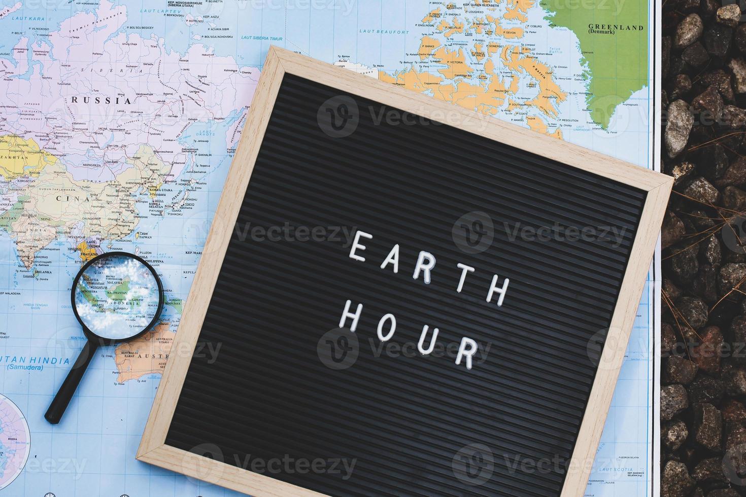 la cita en el tablero de cartas dice la hora de la tierra con una lupa en el mapa mundial foto