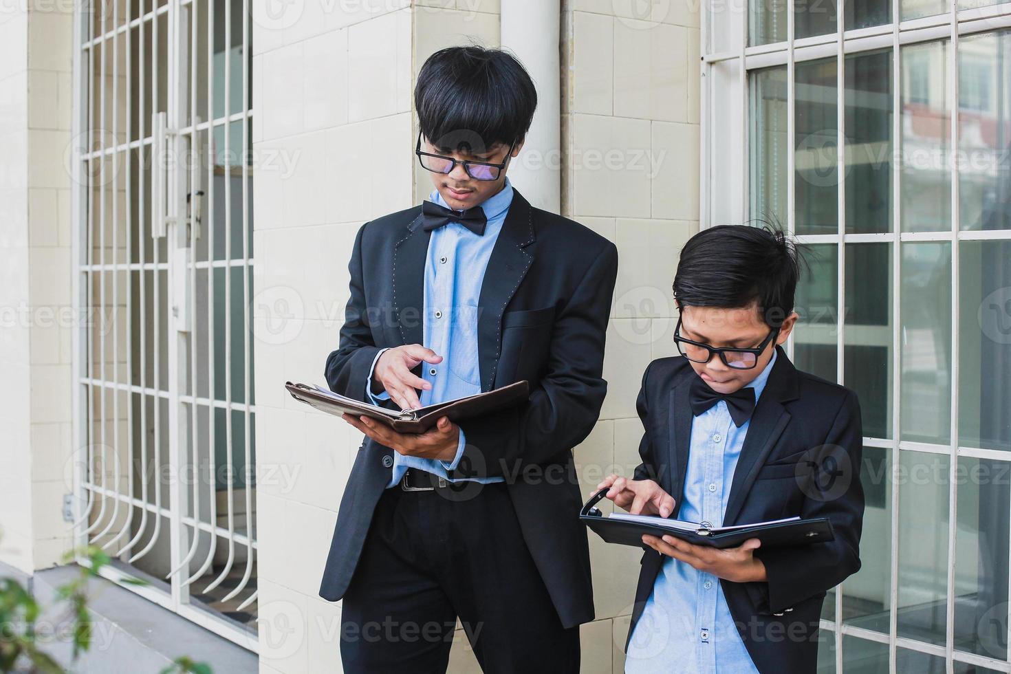 dos adolescentes con aspecto de oficina vintage con gafas, cinta negra y chaqueta de traje negro sosteniendo y leyendo un libro de notas en serio foto