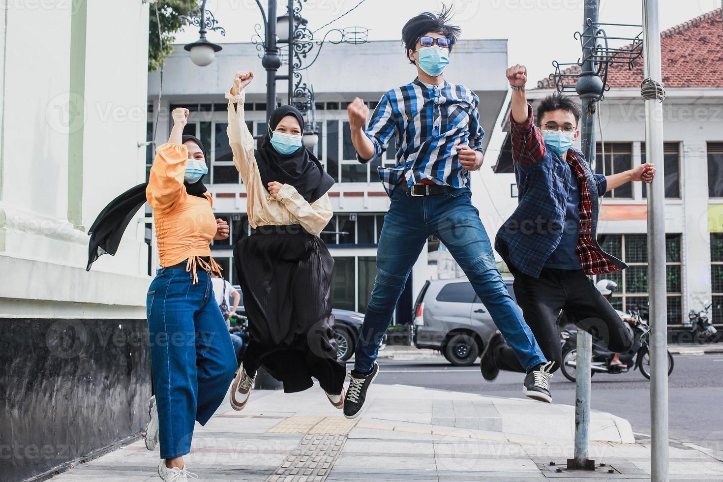 Happy asian friends jumping together outdoors wearing protective masks photo