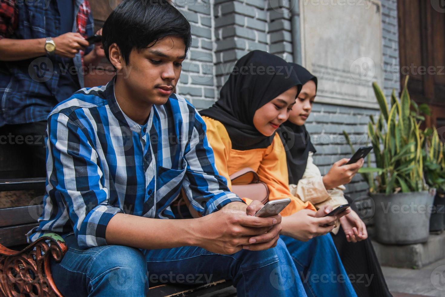 grupo de personas sentadas en el banco usando teléfono móvil. escribiendo en un teléfono inteligente foto