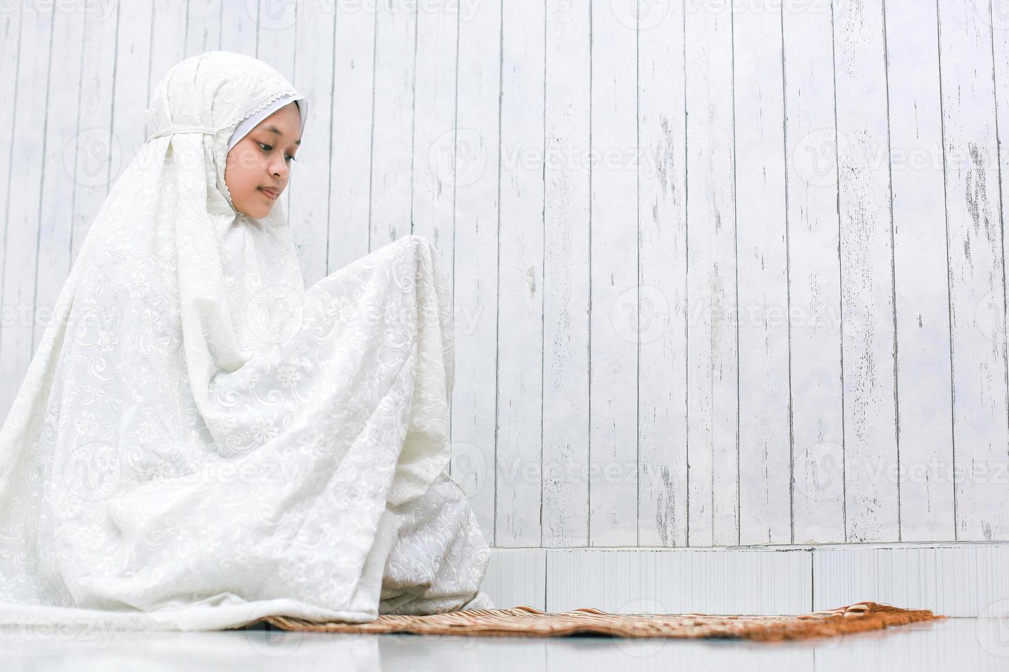 Muslim woman praying to God. Islam girl sitting with begging hand gesture on the prayer mat photo