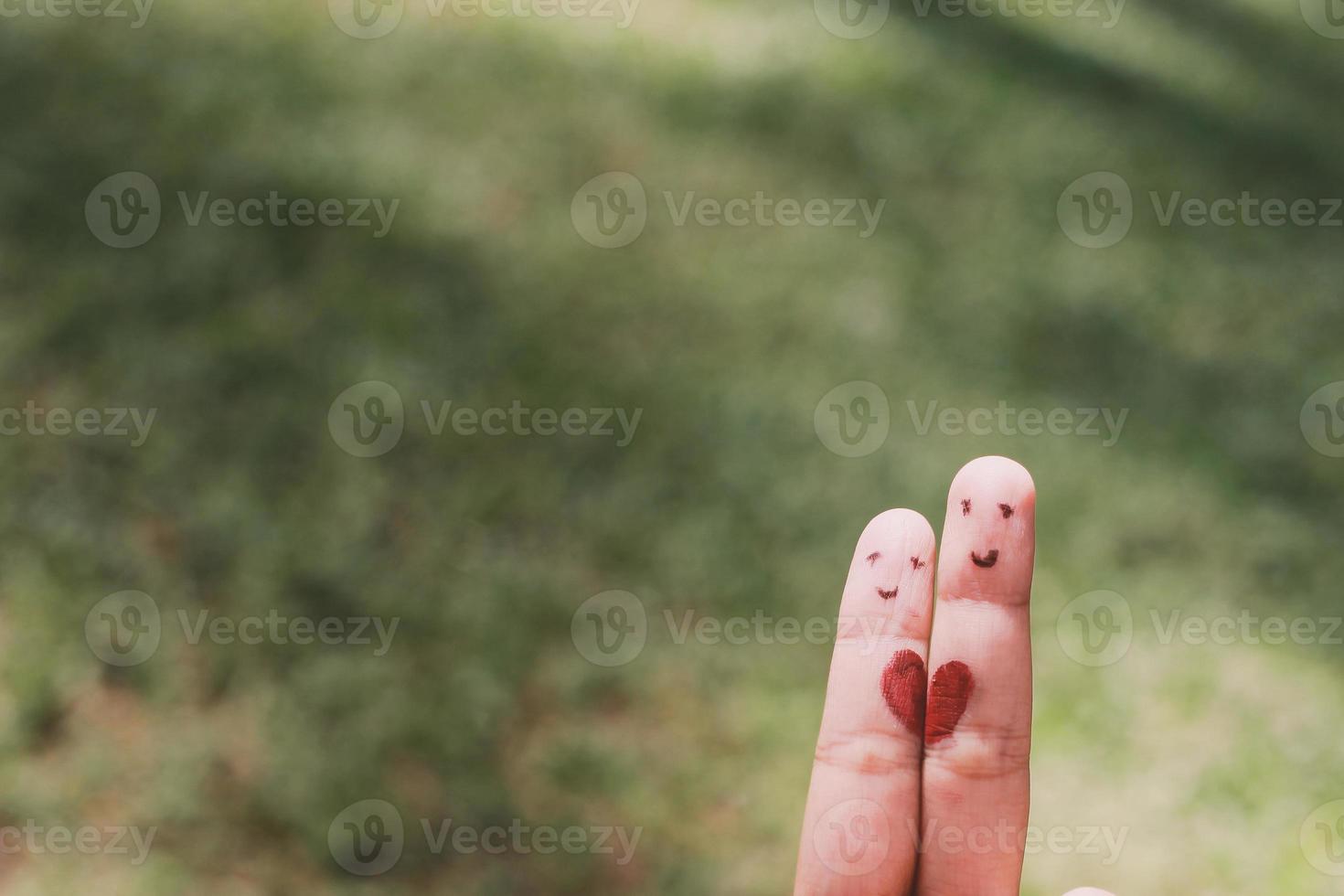 Red heart shape on two fingers with face image while smiling face with nature bokeh background. copy space. Happy couple in love. photo
