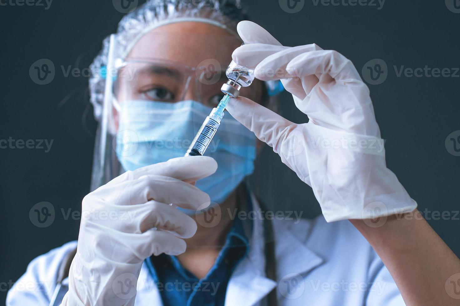 Close-up of doctor or scientist hands in surgical gloves holding vaccine bottle and a syringe with black background. Draws medicine from the vial. Medicine, vaccination, immunization and healthcare photo