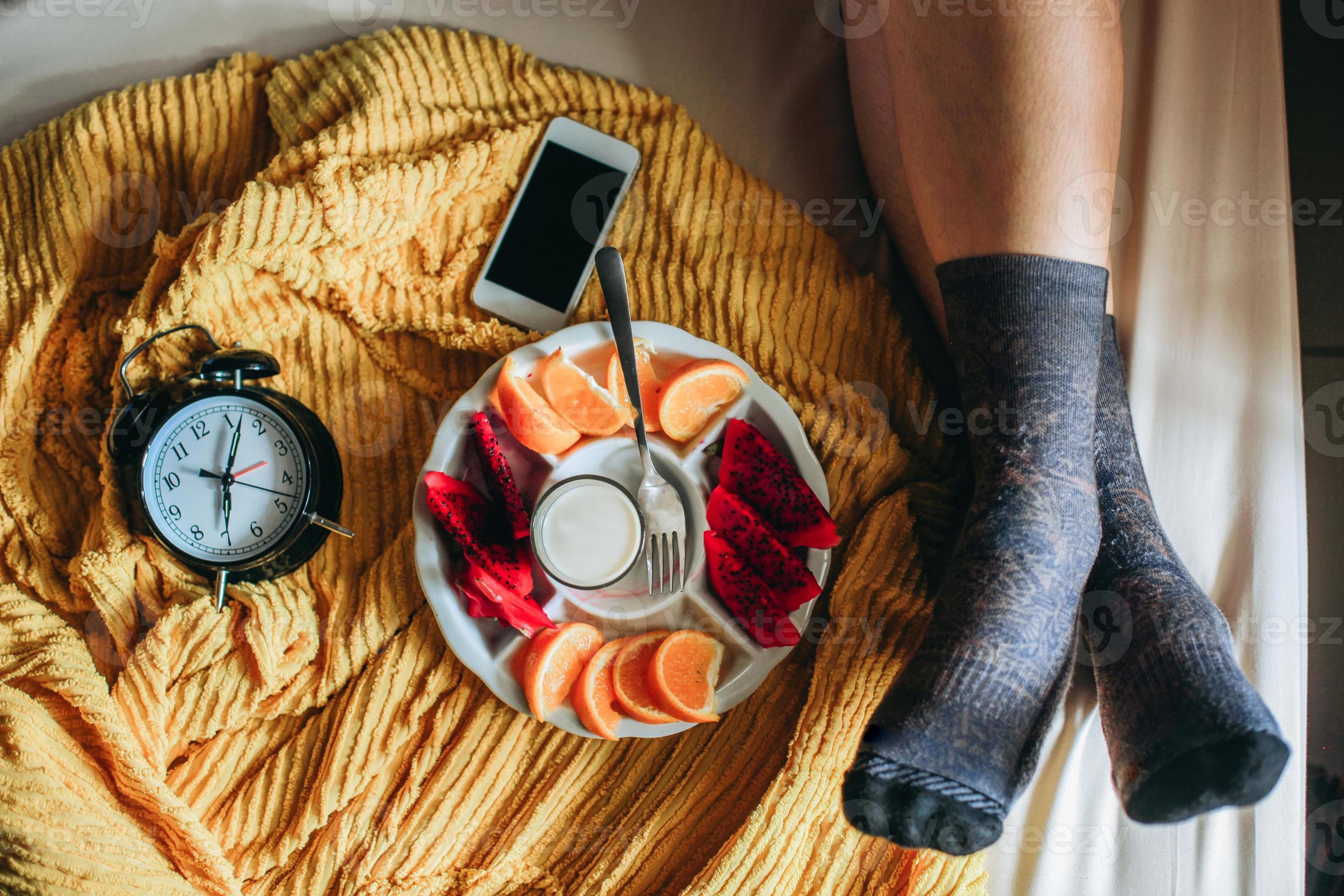 Relax foot in socks on the bed with various fruit, alarm clock and
