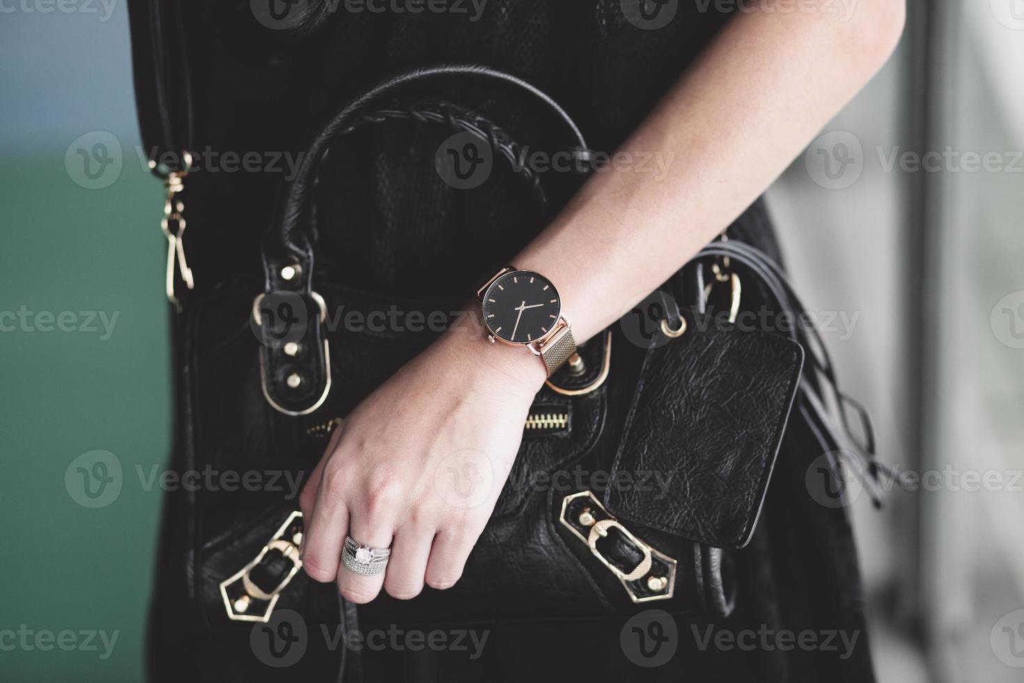 accesorios de lujo en la mano de la mujer con anillo y reloj mientras sostiene una bolsa de mano negra foto